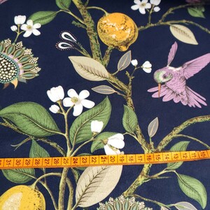 May include: A navy blue fabric with a repeating pattern of hummingbirds, lemons, and white flowers. A measuring tape is placed across the bottom of the fabric.
