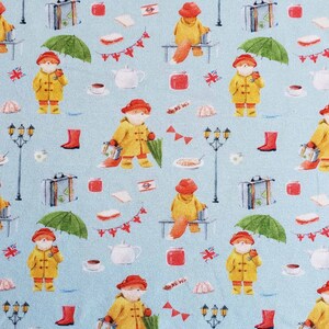 May include: A repeating pattern on a light blue background features a fox character in a yellow raincoat and red hat, holding an umbrella. Other elements include suitcases, tea cups, and British flags. The design has a whimsical, storybook feel.
