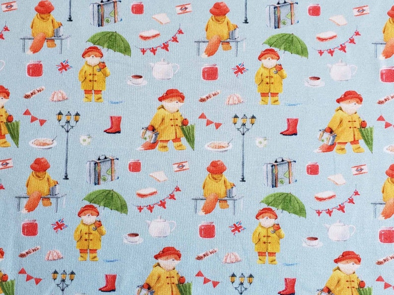 May include: A repeating pattern on a light blue background features a fox character in a yellow raincoat and red hat, holding an umbrella. Other elements include suitcases, tea cups, and British flags. The design has a whimsical, storybook feel.