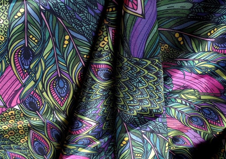 May include: A colorful fabric with a peacock feather pattern. The fabric is a dark blue with green, pink, and yellow accents. The feathers are detailed with intricate designs.