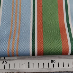 May include: Striped fabric with alternating bands of light blue, white, orange, green, and red. The fabric is folded over a ruler marked with the numbers 50 and 60.