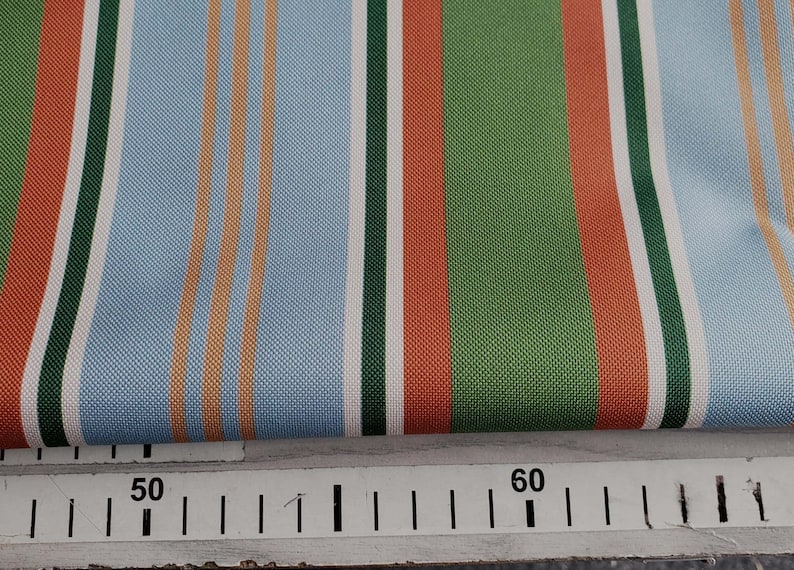 May include: Striped fabric with alternating bands of light blue, white, orange, green, and red. The fabric is folded over a ruler marked with the numbers 50 and 60.