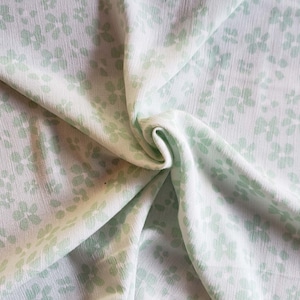 Pu&ograve; includere: Tessuto bianco con un motivo floreale verde chiaro. Il tessuto &egrave; piegato e drappeggiato.