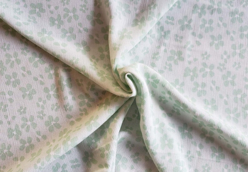Pu&ograve; includere: Tessuto bianco con un motivo floreale verde chiaro. Il tessuto &egrave; piegato e drappeggiato.