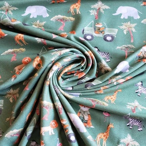 May include: Green fabric with a repeating pattern of safari animals, including elephants, zebras, giraffes, lions, and a jeep. The fabric is folded and draped, showing the pattern.