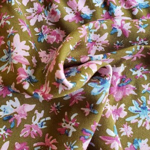 Pu&ograve; includere: Primo piano di un tessuto con motivo floreale. Il tessuto &egrave; di colore verde oliva spento con fiori rosa e blu.
