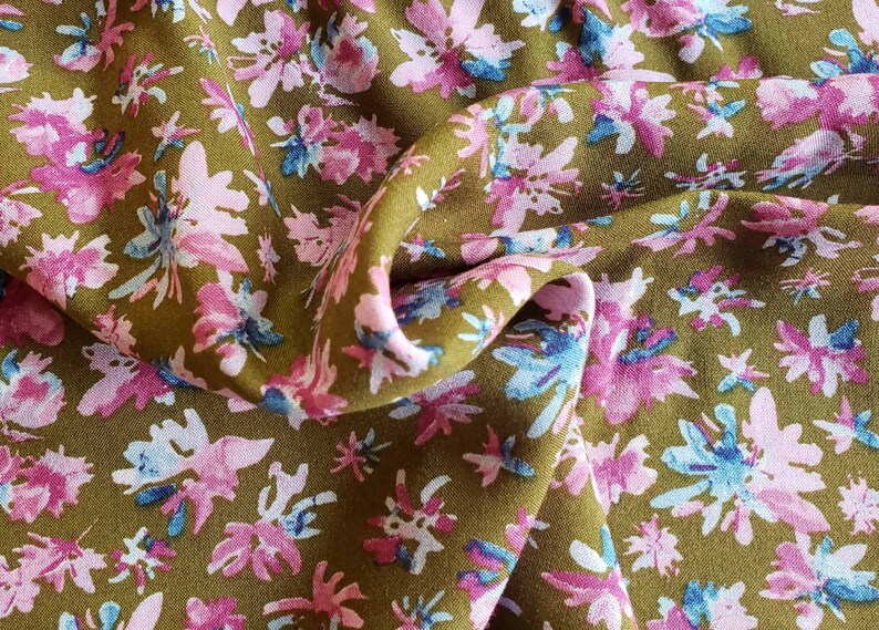 Pu&ograve; includere: Primo piano di un tessuto con motivo floreale. Il tessuto &egrave; di colore verde oliva spento con fiori rosa e blu.