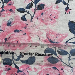 May include: A close-up of a gray fabric with a pink and blue floral print. The fabric has a ruler on top of it with the words "initiative Shatter Resistant" printed on it.