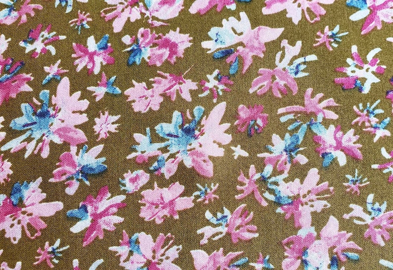 Pu&ograve; includere: Un tessuto marrone con un motivo ripetitivo di fiori stilizzati rosa, blu e bianchi. I fiori sono astratti e hanno un aspetto acquerellato.