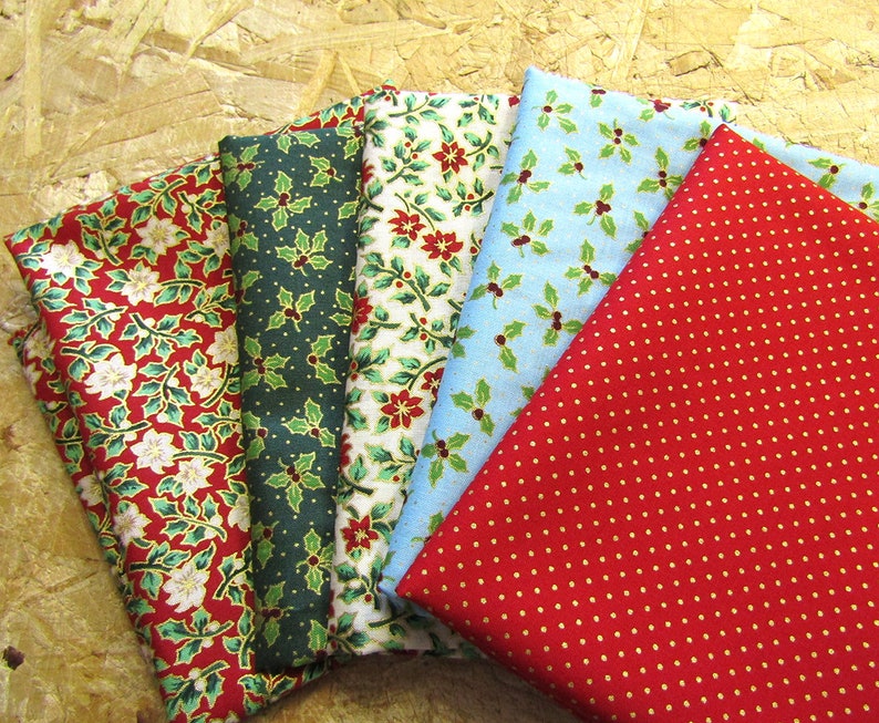 K&ouml;nnte beinhalten: F&uuml;nf Stoffmuster mit Weihnachtsmotiven. Die Muster sind rot, gr&uuml;n, blau, wei&szlig; und gold. Die Muster umfassen Stechpalmenbl&auml;tter, Weihnachtssterne und Punkte.