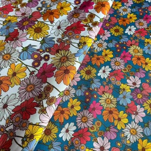 Op de afbeelding: Een textielstof met een dicht bloemenpatroon van madeliefjes in tinten rood, oranje, geel, roze en lichtblauw. Het ontwerp wordt gepresenteerd op twee verschillende achtergrondkleuren: een helder wit aan de linkerkant en een levendig blauwgroen aan de rechterkant.