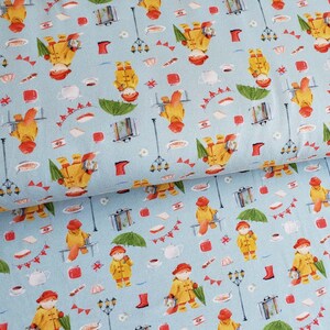 May include: Light blue fabric with a repeating pattern of a bear in a yellow raincoat, red hat, and boots. The design includes umbrellas, suitcases, and street lamps, creating a whimsical, storybook theme.