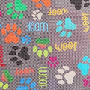 May include: Gray fabric with a pattern of colorful paw prints and the word "WOOF" in various colors. The paw prints are in shades of pink, orange, green, blue, and black, creating a playful design.