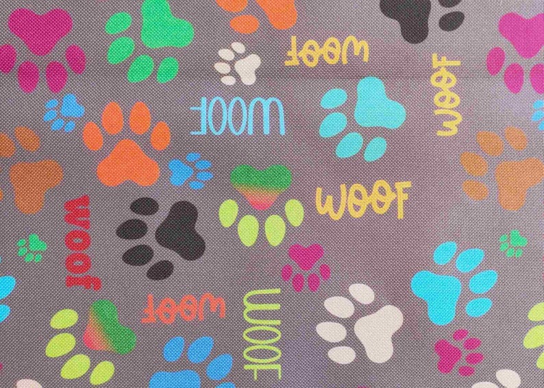 May include: Gray fabric with a pattern of colorful paw prints and the word "WOOF" in various colors. The paw prints are in shades of pink, orange, green, blue, and black, creating a playful design.