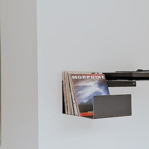 May include: A black metal wall shelf with a record player on top and a stack of vinyl records underneath. The record cover on top reads "MORPHINE".