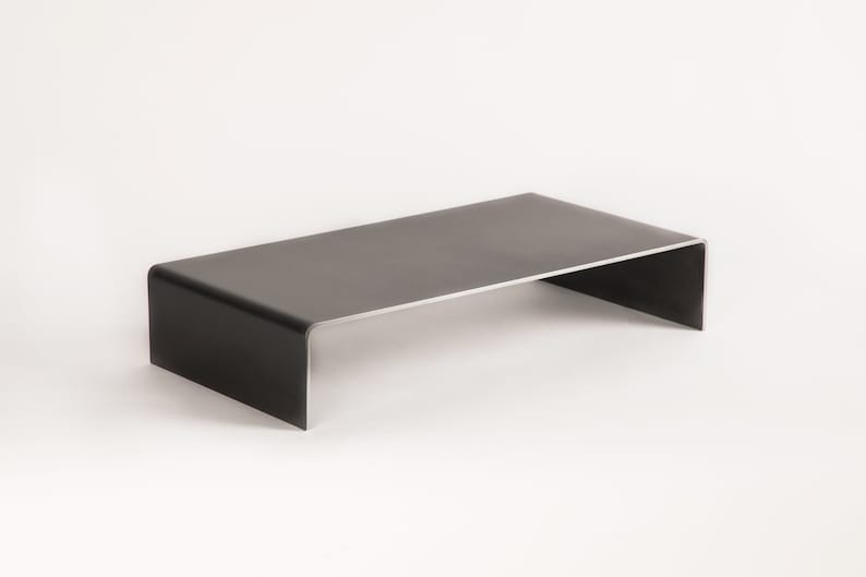 Pu&ograve; includere: Un tavolino da caff&egrave; in metallo nero con un piano rettangolare e un bordo curvo. Il tavolo &egrave; realizzato in un unico pezzo di metallo e ha un design moderno.