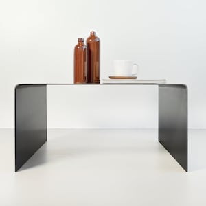 May include: A black metal coffee table with a rectangular top and a unique open frame design. Two brown glass bottles and a white ceramic mug are placed on the table.