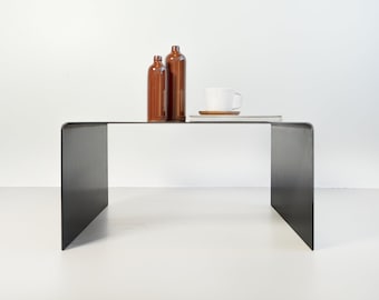 Op de afbeelding: Een zwarte metalen salontafel met een rechthoekig blad en een uniek open frame ontwerp. Twee bruine glazen flessen en een witte keramische mok staan op de tafel.