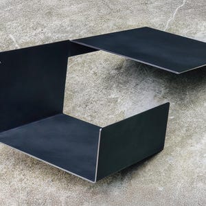 May include: A black metal shelf unit with a removable top panel. The shelf unit is made of metal and has a simple, modern design.