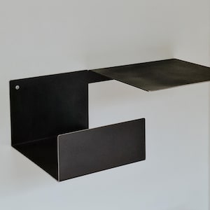 May include: A black metal shelf unit with two shelves. The top shelf is a floating shelf that is attached to the wall. The bottom shelf is a rectangular shelf that is attached to the wall with a bracket.