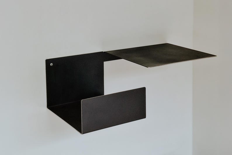 May include: A black metal shelf unit with two shelves. The top shelf is a floating shelf that is attached to the wall. The bottom shelf is a rectangular shelf that is attached to the wall with a bracket.