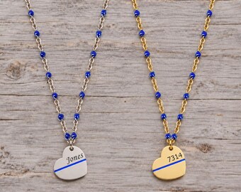 May include: Two necklaces featuring chains with small blue beads. One necklace has a silver-toned metal chain and a heart-shaped pendant engraved with the name Jones and a blue line. The other has a gold-toned chain and a heart pendant with 7314.