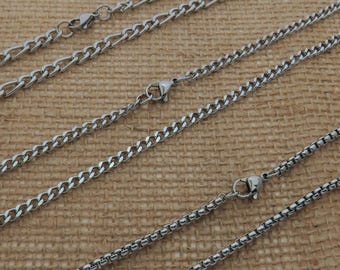 May include: Close-up of several silver chain necklaces with various link styles. The chains are displayed on a textured, beige surface. Each necklace has a clasp for easy wear.
