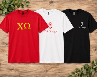 May include: Three short-sleeve crew neck t-shirts in red, white, and black. The red shirt features yellow Greek letters Chi Omega. The white shirt displays a red owl graphic and the text Chi Omega. The black shirt has a small white owl and text.