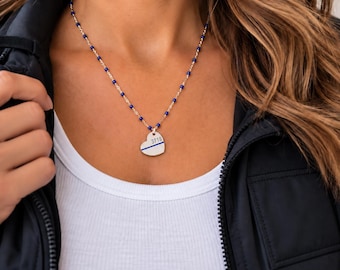 May include: A silver-toned heart-shaped pendant necklace featuring the number 3719 and a thin horizontal blue line. The chain is composed of silver-toned links interspersed with small, round, vibrant blue beads that match the line on the pendant.