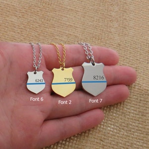 May include: Three silver and gold necklaces with a blue line and a shield pendant. The pendants have the numbers 6243, 7159, and 8216 on them. The necklaces are labelled with the font numbers 6, 2, and 7.