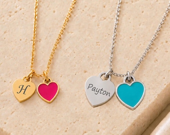 May include: Two necklaces with delicate chains. The gold-tone necklace features a heart charm engraved with the letter H and a solid hot pink heart charm. The silver-tone necklace features a heart charm engraved with the name Payton and a turquoise heart.