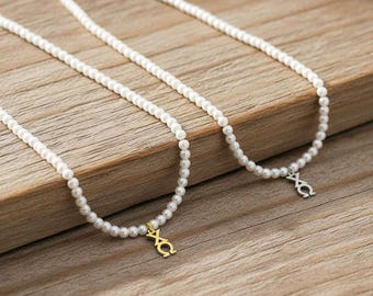 May include: Two necklaces made of small white spherical beads. One necklace features a gold-toned metal charm shaped like the Greek letters Chi and Omega. The second necklace features a silver-toned metal charm with the same Greek letter design.