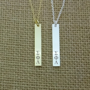May include: Two vertical bar necklaces with a gold and silver chain. The bars have the Greek letters Sigma Phi Lambda engraved on them.