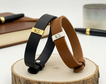 May include: Two leather bracelets, one black and one brown, each featuring a metal accent piece engraved with the Greek letters KΣ. The black bracelet has a gold-toned metal bar, while the brown bracelet has a silver-toned metal bar.