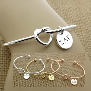 May include: Silver, gold, and rose gold knot bracelets with a round charm that says "ΣΛΓ".