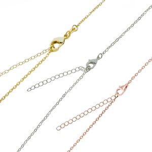 May include: Close-up of three delicate chain necklaces in gold, silver, and rose gold. Each necklace features a lobster clasp and an adjustable chain. The chains are displayed against a white background.