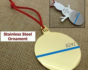 May include: Gold stainless steel bauble ornament with a blue line across the centre. The ornament is shaped like a Christmas ball and has the number 8241 printed on it. The ornament is hanging from a red cord.