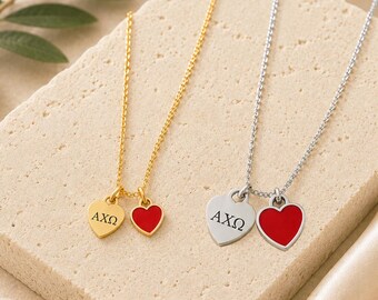 May include: Two necklaces, one gold-toned and one silver-toned, each featuring two heart-shaped charms. One charm on each necklace is engraved with the Greek letters AXΩ, while the other charm is filled with a solid red enamel color.