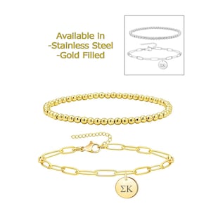 May include: Two gold bracelets, one with a chain design and a charm with the letters "ΣΚ" and the other with a beaded design. Available in stainless steel or gold filled.