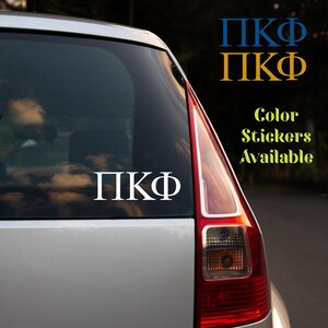 May include: White vinyl sticker with the Greek letters ΠΚΦ on a car window. The sticker is displayed on the rear window of a silver car. Additional text in blue and gold reads "ΠΚΦ" and "Color Stickers Available."