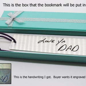 May include: A silver bookmark with a handwritten message "LOVE YA DAD" in a turquoise gift box. The bookmark is in a gift box with a silver ribbon.