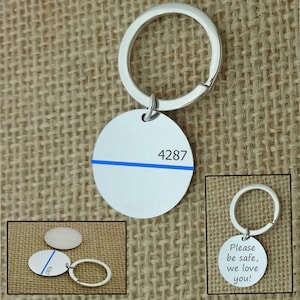 Könnte beinhalten: Silberner Schlüsselanhänger mit einer blauen Linie und der Nummer 4287, die auf ein rundes Schild graviert ist. Der Schlüsselanhänger hat auch ein kleineres Schild mit der Aufschrift "Bitte pass auf dich auf, wir lieben dich!"