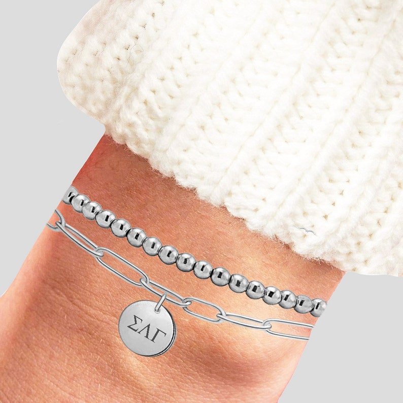 May include: A silver chain bracelet with a silver charm that says "&Sigma;&Lambda;&Gamma;" and a silver beaded bracelet.