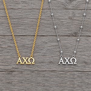 Può includere: Una collana color oro e una collana color argento, entrambe con le lettere greche Alfa, Chi e Omega come ciondolo. La collana dorata ha una catena a maglie standard, mentre quella argentata presenta una catena con piccole perline di metallo.