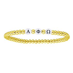Può includere: Braccialetto dorato con perline bianche con le lettere greche Alfa, Phi e Omega. Il braccialetto è composto da piccole perline rotonde color oro. Le perline bianche con le lettere sono al centro.