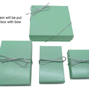 May include: Four mint green gift boxes of varying sizes, each tied with a silver string bow. The largest box is square, while the others are rectangular. Text in the image reads: "Your item will be put in this box with bow."