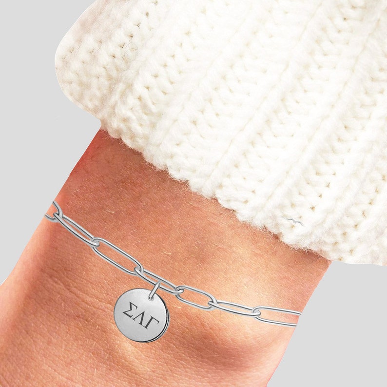 May include: A silver chain bracelet with a round charm that says "&Sigma;&Lambda;&Gamma;" on it.