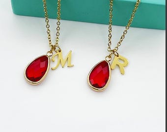 May include: Two gold-colored necklaces with teardrop-shaped red pendants and initial charms. One necklace has an "M" charm, the other an "R" charm. The pendants and charms are suspended from delicate gold chains.