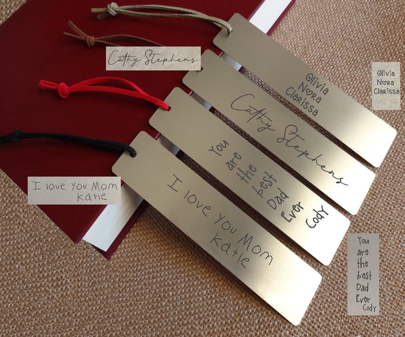 May include: Four silver metal bookmarks with personalised text. The bookmarks have black, red and brown leather straps. The text on the bookmarks reads "I love you Mom Katie", "You are the best Dad Ever Cody", "Cathy Stephens", and "Olivia Nora Clarissa".