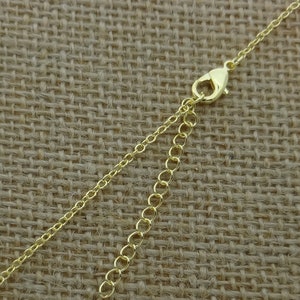 May include: A gold-colored necklace chain with a lobster clasp and an extender chain. The chain is made of small, delicate links. The background is a textured, tan fabric.